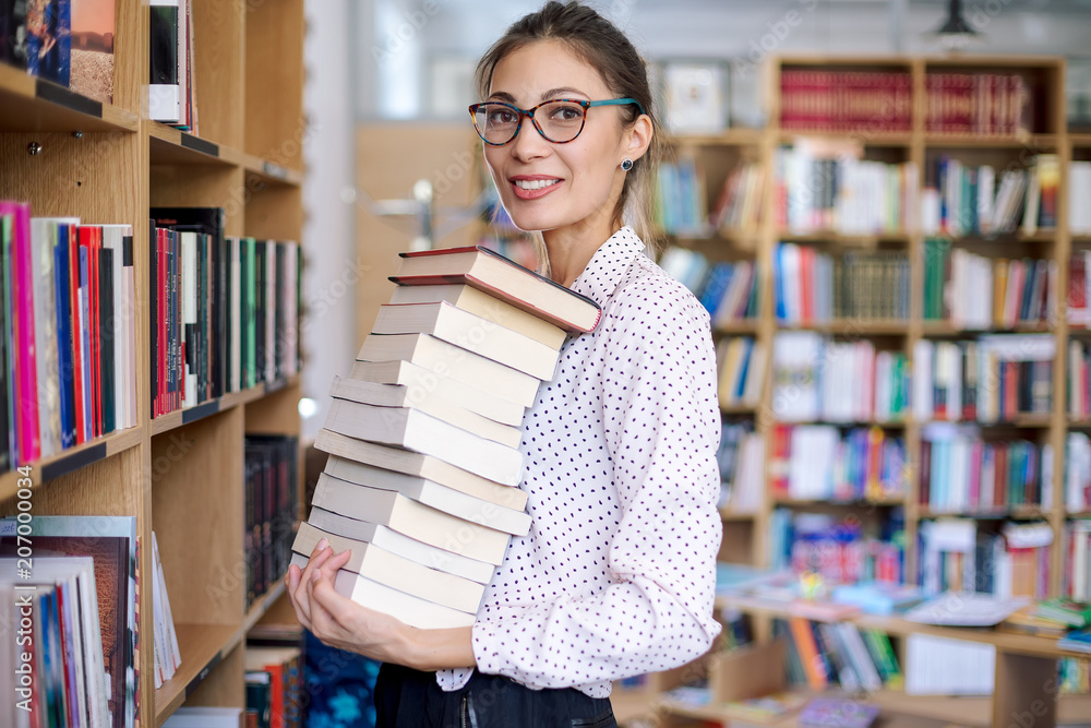 Portrait of young woman with a stack of books in library Portrait of young woman with a stack of books in library