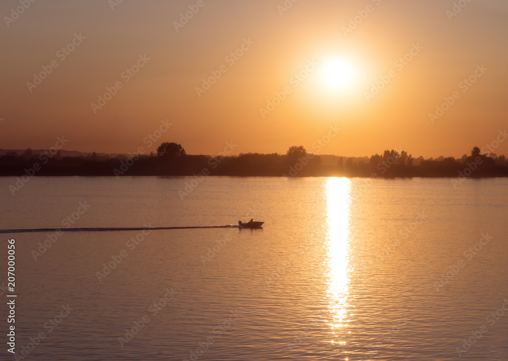 The boat floats on the Tom river in the light of sunset