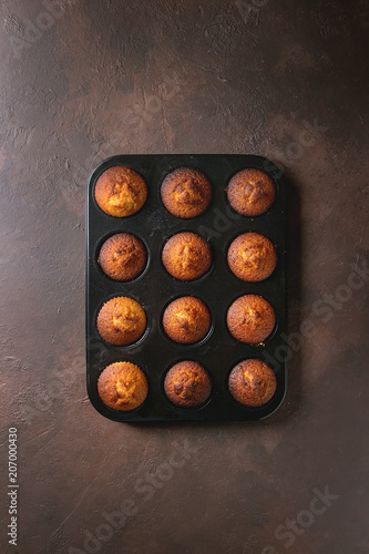 Fresh baked homemade lemon cakes muffins in black teflon baking dish over dark texture background. Top view, space.
