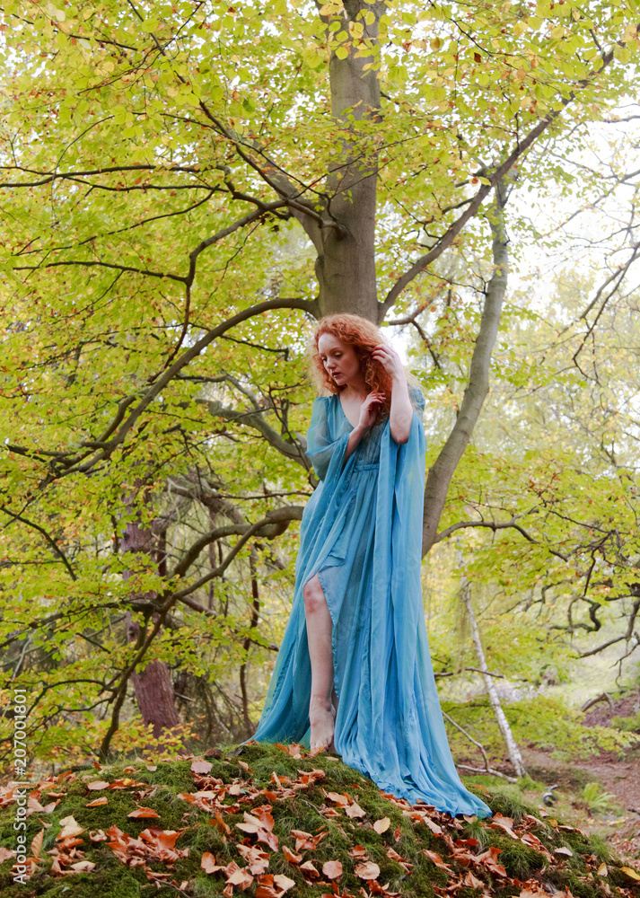 Beautiful woman with long red hair posing in sheer turquoise dress against autumn trees Beautiful woman with long red hair posing in sheer turquoise dress against autumn trees