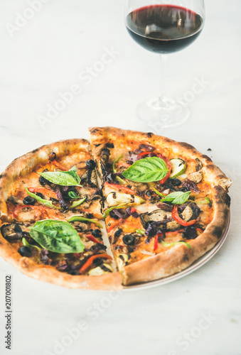 Summer dinner or lunch. Freshly baked Italian vegetarian pizza with vegetables, fresh basil and glass of red wine over white marble table, copy space