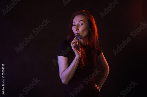 young woman smoking electronic cigarette on dark background