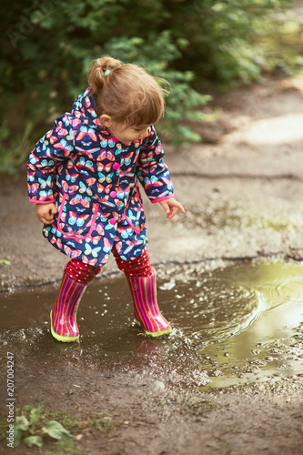 Fototapeta Naklejka Na Ścianę i Meble -  Little girl in gumboots has fun walking in the pools after the rain