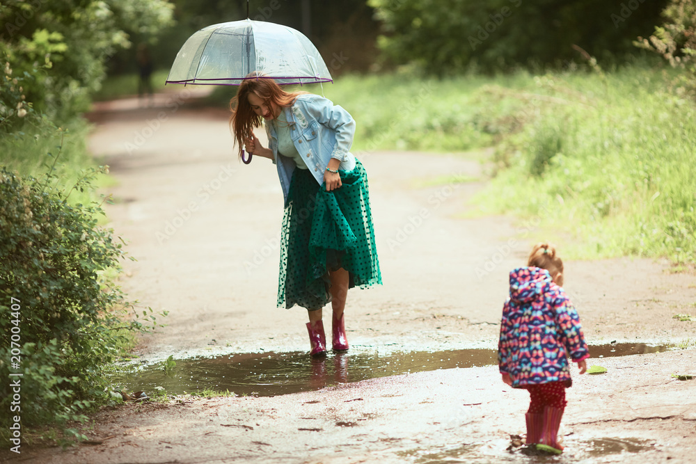 Beautiful young woman in green skirt has fun walking with little girl  in gumboots on pools after the rain