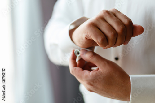 Close-up hands of businessman with expensive watches buttons cuff link on French cuffs sleeves luxury white shirt. The groom is preparing for the wedding, going to meet with the bride