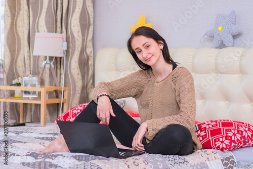 Portrait of beautiful brunette freelancer girl working with laptop on bed at home. photo