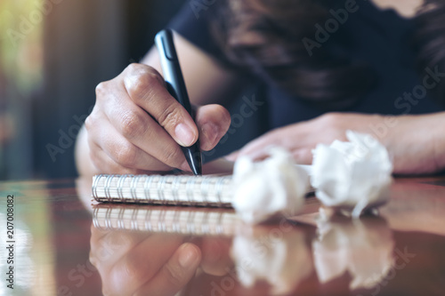 Closeup image of a businesswoman working and writing down on a white blank notebook with screwed up papers on table