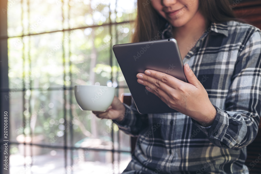 Closeup image of a woman holding and using tablet pc while drinking coffee in cafe Closeup image of a woman holding and using tablet pc while drinking coffee in cafe