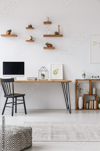 Patterned pouf in minimal workspace interior with black chair at table with computer monitor. Real photo
