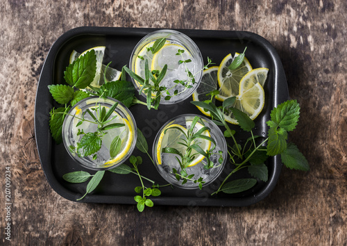 Garden herbs lemonade. Infused water with lemon, rosemary, thyme, sage and mint on wooden background, top view. Summer cool drink