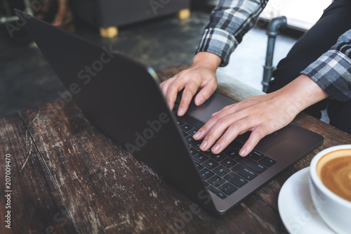 Closeup image of a woman working and typing on laptop keyboard with coffee cup on the table