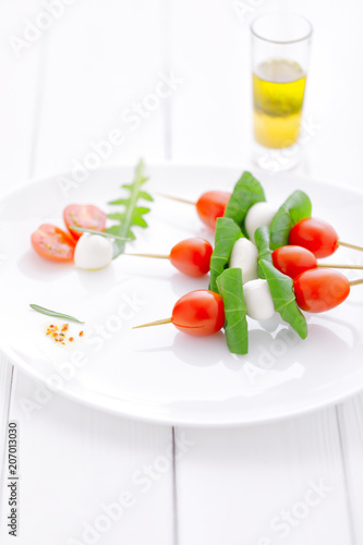 cherry tomatoes with basil and mozzarella cheese on .wooden skewers placed on a white plate and white wooden table