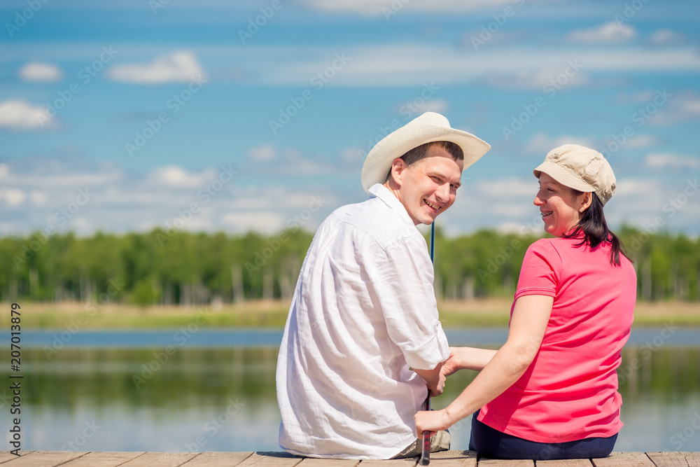 happy couple with a fishing rod sitting on a wooden pier near the lake happy couple with a fishing rod sitting on a wooden pier near the lake