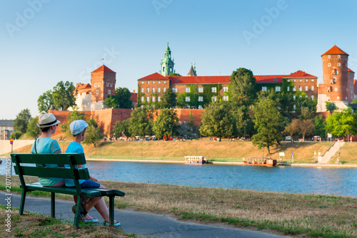 Krakow, Poland - August 11, 2017: tourists on the bench admire the beautiful Wawel Castle in Krakow