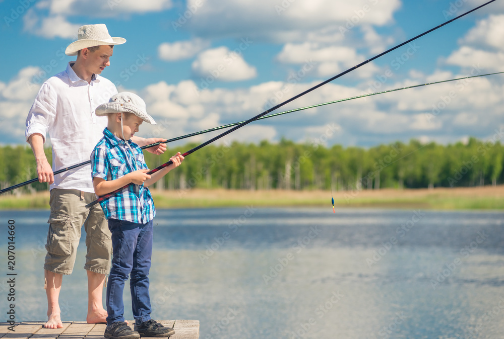 father and son with fishing rods on a wooden pier near the lake on a sunny day father and son with fishing rods on a wooden pier near the lake on a sunny day