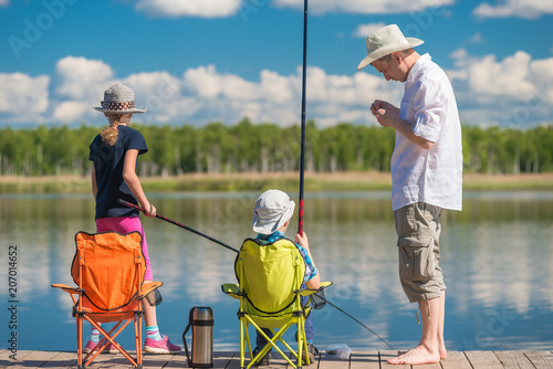 father teaches his children to fish on a fishing pole at the pier by the lake