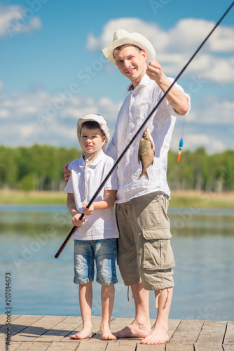 vertical portrait of the father and son on the pier with a big fish on the hook, fishing on the lake
