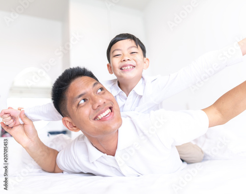 Happy father playing with son while lying on the bed at home