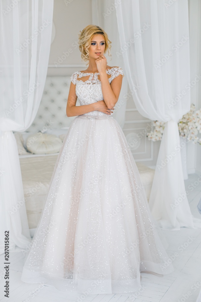 A bride with hairstyle and make up in gougeous wedding dress preparing for the wedding. A portrait of beautiful girl with blond hair and blue eyes in studio with flowers A bride with hairstyle and make up in gougeous wedding dress preparing for the wedding. A portrait of beautiful girl with blond hair and blue eyes in studio with flowers