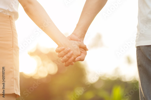 Lovers in the park tenderly hold hands together, blurred background.