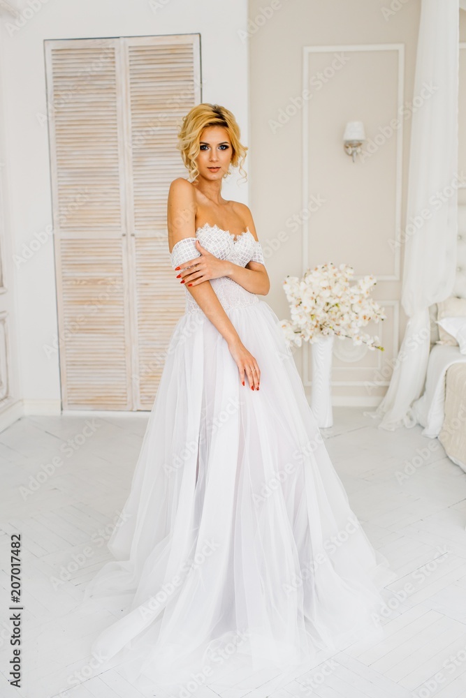 A bride with hairstyle and make up in gougeous wedding dress preparing for the wedding. A portrait of beautiful girl with blond hair and blue eyes in studio with flowers A bride with hairstyle and make up in gougeous wedding dress preparing for the wedding. A portrait of beautiful girl with blond hair and blue eyes in studio with flowers