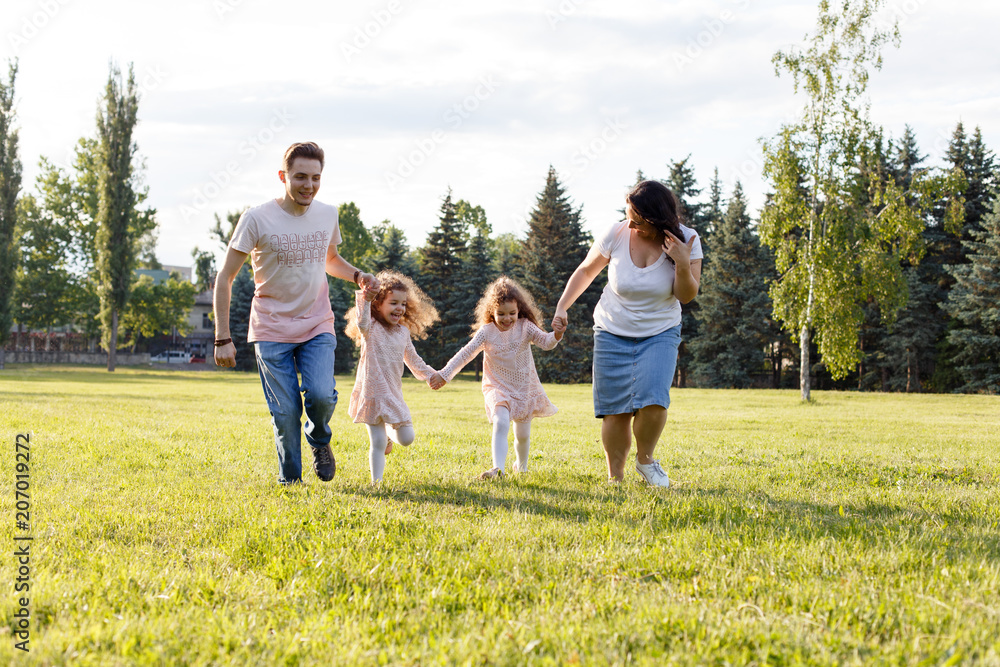 Fototapeta premium Smiling Family Running Across Summer Field Together, happy family with twin toddler girls