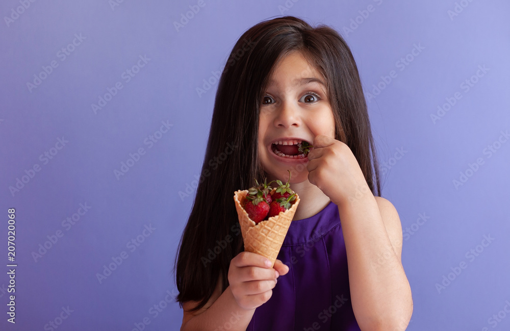 Cute little child girl eating fresh strawberries from ice cream horn. Healthy food. Summer time. Cute little child girl eating fresh strawberries from ice cream horn. Healthy food. Summer time.