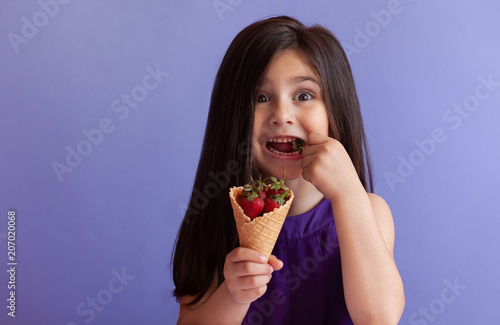 Cute little child girl eating fresh strawberries from ice cream horn. Healthy food. Summer time.