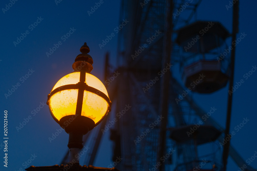 atmospheric image of old fashioned vintage yellow lantern with big ferris wheel in background at night