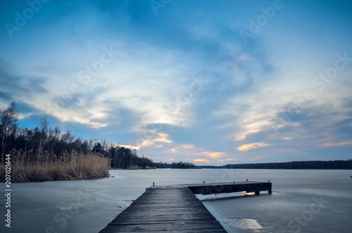 Evening winter landscape. Wooden pier over a beautiful frozen lake. © shadowmoon30