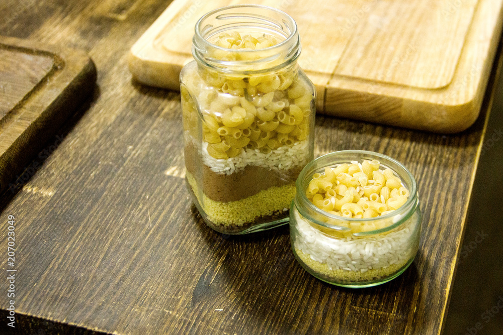raw pasta in two glass jars decor on the wooden table background with boards raw pasta in two glass jars decor on the wooden table background with boards