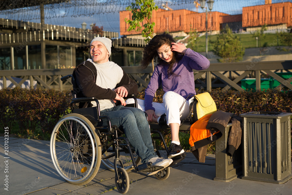 Obraz premium Happy couple - disabled man in wheelchair talking with attractive young woman enjoing the sunset