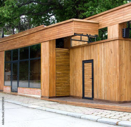 A clean wooden facade of a shop near a road in the background of a tree