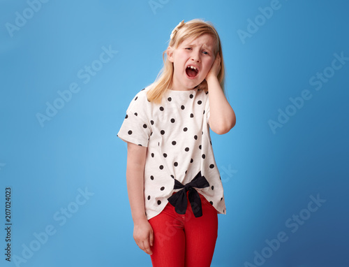 unhappy modern girl in red pants on blue with earache