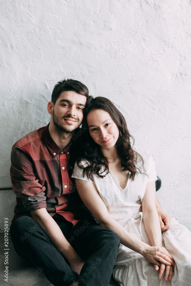 charismatic couple at a photo shoot in European style. Hugging and smiling looking at each other. The casual look and the light airy dress of the girl. the loft Studio, and a beautiful girl charismatic couple at a photo shoot in European style. Hugging and smiling looking at each other. The casual look and the light airy dress of the girl. the loft Studio, and a beautiful girl