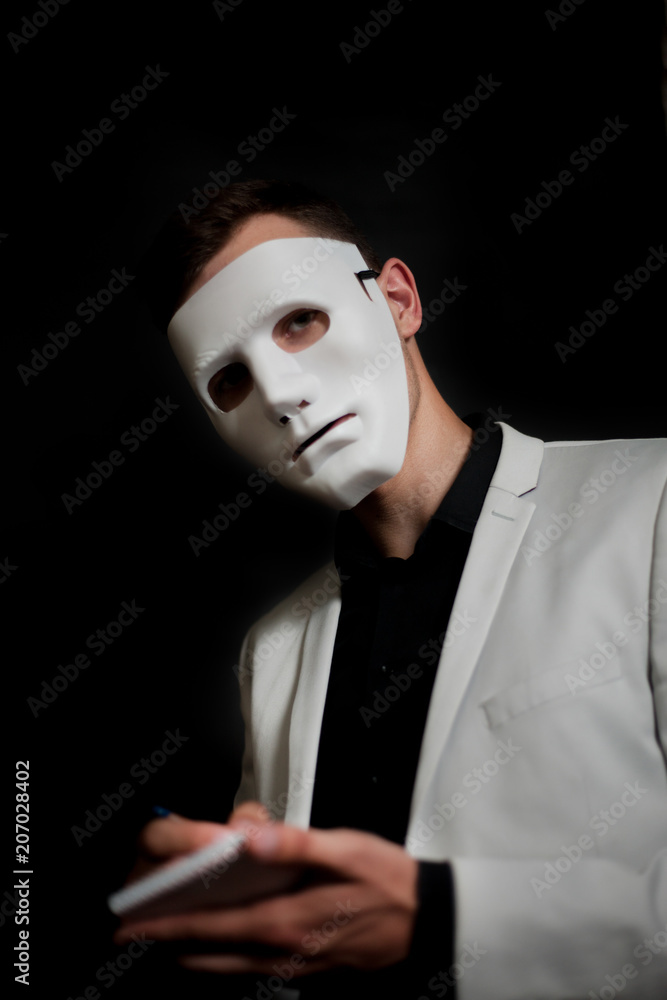 Man in a white mask in a white jacket on a black background writes in a notebook Man in a white mask in a white jacket on a black background writes in a notebook