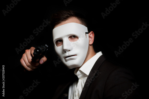 A man in a white mask on a black background, threatens with a gun