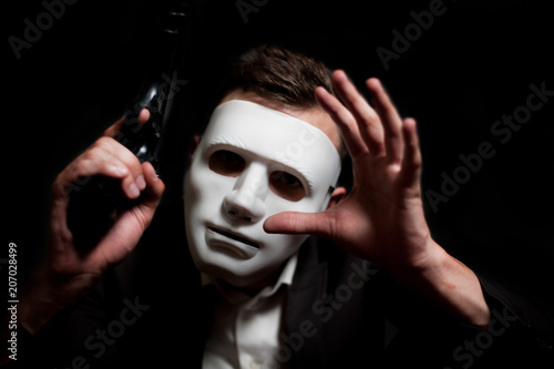 Close-up of a man in a white mask, holding a gun in his hand
