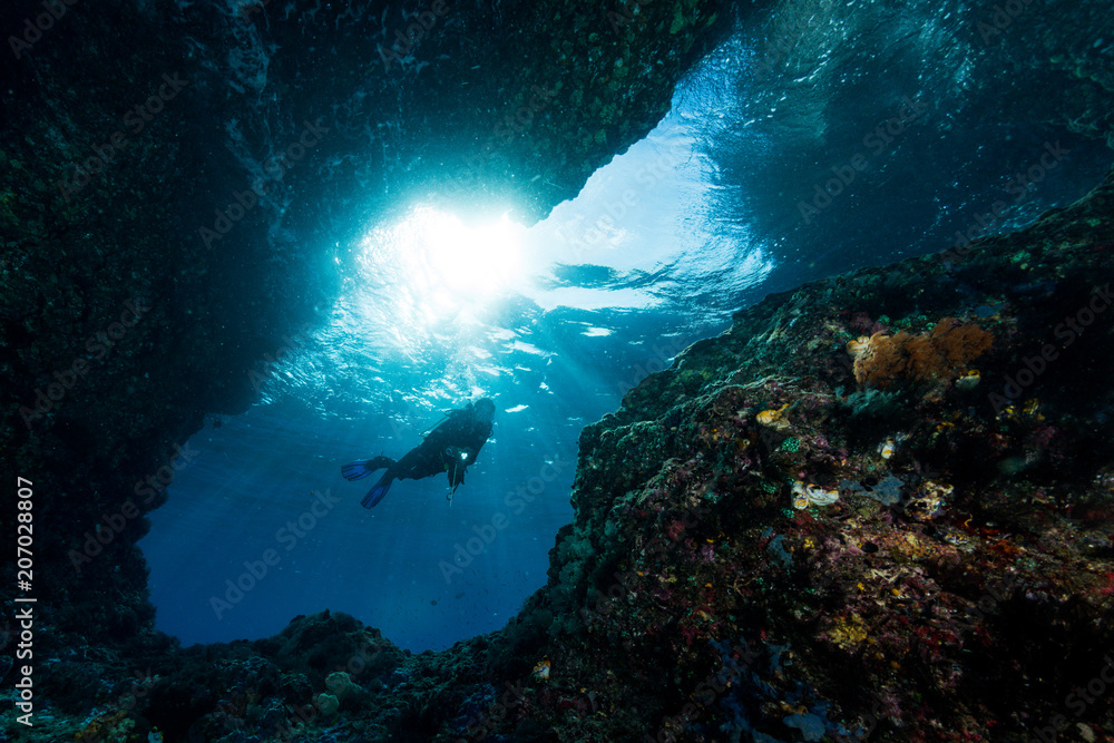 woman diver underwater at the entrance of a cave with sunrays woman diver underwater at the entrance of a cave with sunrays