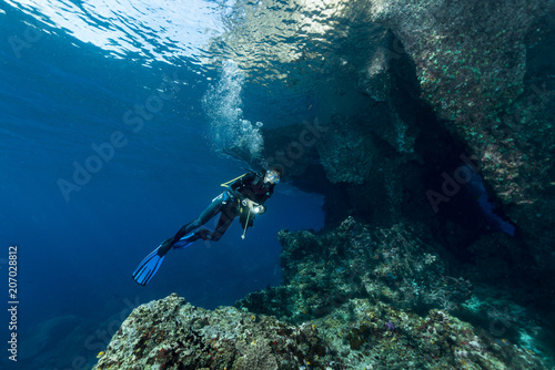 woman diver underwater at the entrance of a cave with sunrays