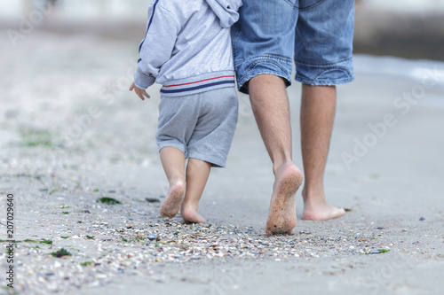 the feet of dad and child going for a walk on a coast