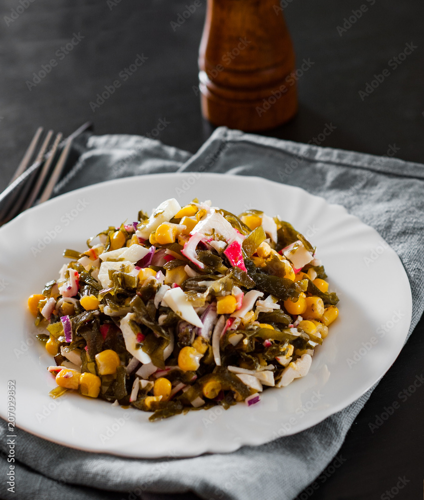 Seaweed Chuka sea kale salad with corn , crab sticks, eggs, onion on white plate on dark wooden table Seaweed Chuka sea kale salad with corn , crab sticks, eggs, onion on white plate on dark wooden table