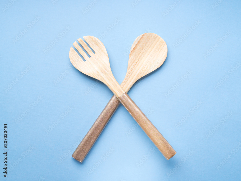 Minimal cooking, eating concept on blue background with wooden salad fork and spoon. Minimal cooking, eating concept on blue background with wooden salad fork and spoon.