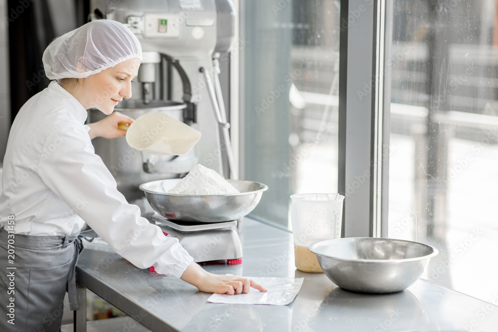 Woman confectioner in uniform weighing ingredients for pastry working at the bakery manufacturing Woman confectioner in uniform weighing ingredients for pastry working at the bakery manufacturing