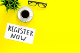 Membership concept. Template for registration. Register now hand lettering iconon word desk with glasses, coffee, plant on yellow background top view space for text
