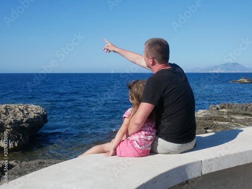 Father with his little daughter sitting on a sea cost (Favignana, Sicily, Italy).