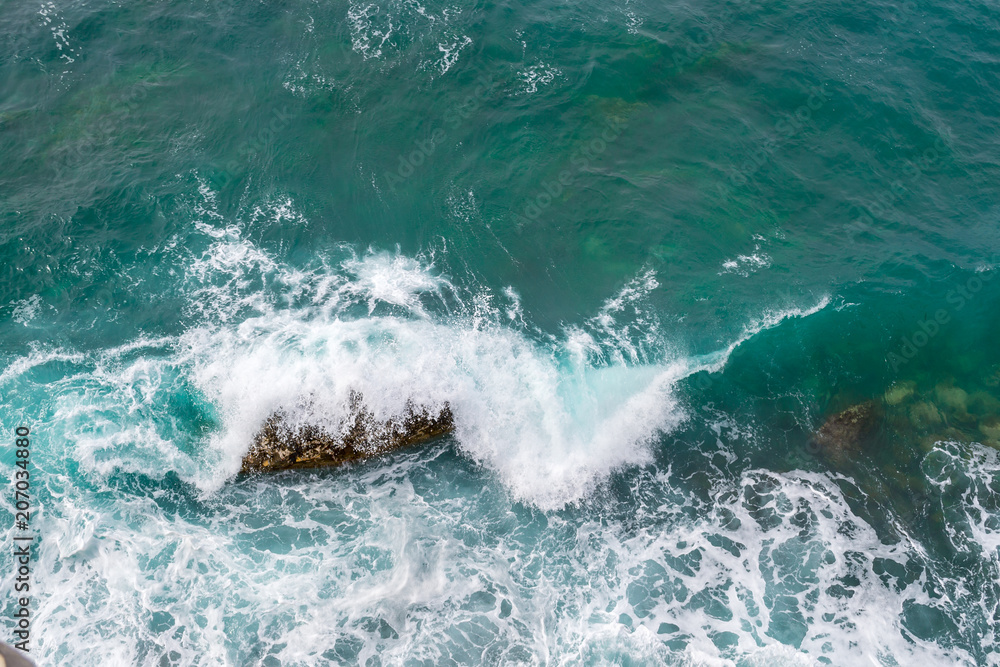 Big waves breaking on the shore. Waves and white foam. Coastal stones. View from above. The marine background is green