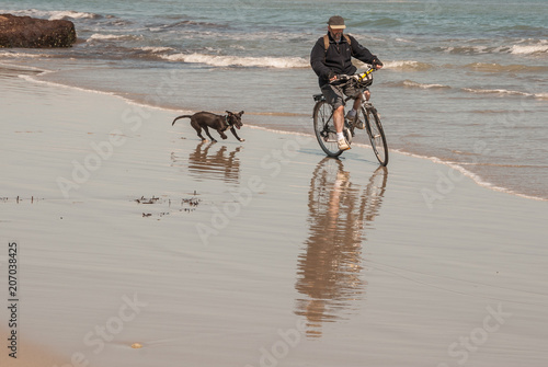 Man on bicycle has fun with his dog on the beach