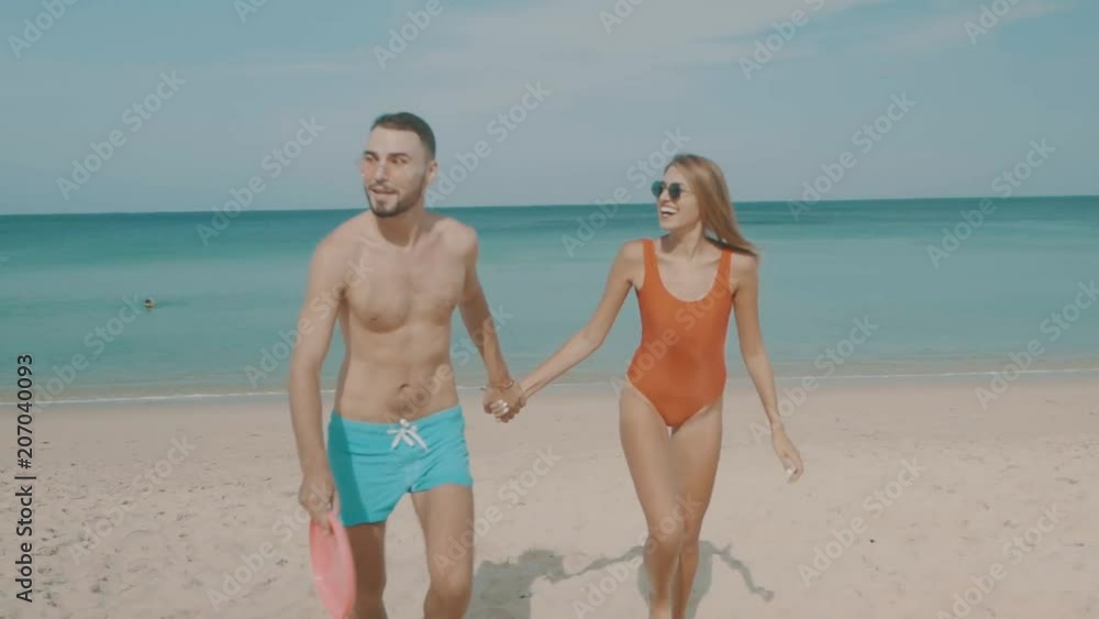 Happy couple playing with frisbee flying disc on the beach during sunny summer day Happy couple playing with frisbee flying disc on the beach during sunny summer day