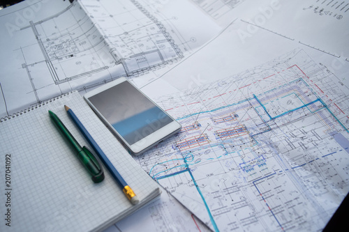 Green pen, blue pencil, white cellphone, notepad and some paper draws of a house (home) are laying down on white table. All staff is for a architecture negotiation.